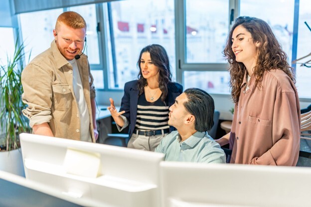 A leader talking to his team, who are gathered around a computer, who has used DISC to help understand the impact of his behaviour on his team.